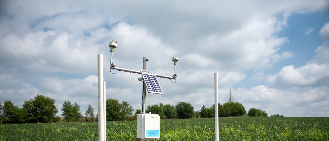 An IFC hydrostation stationed in a field, with deep green foliage around it and cloudy skies behind